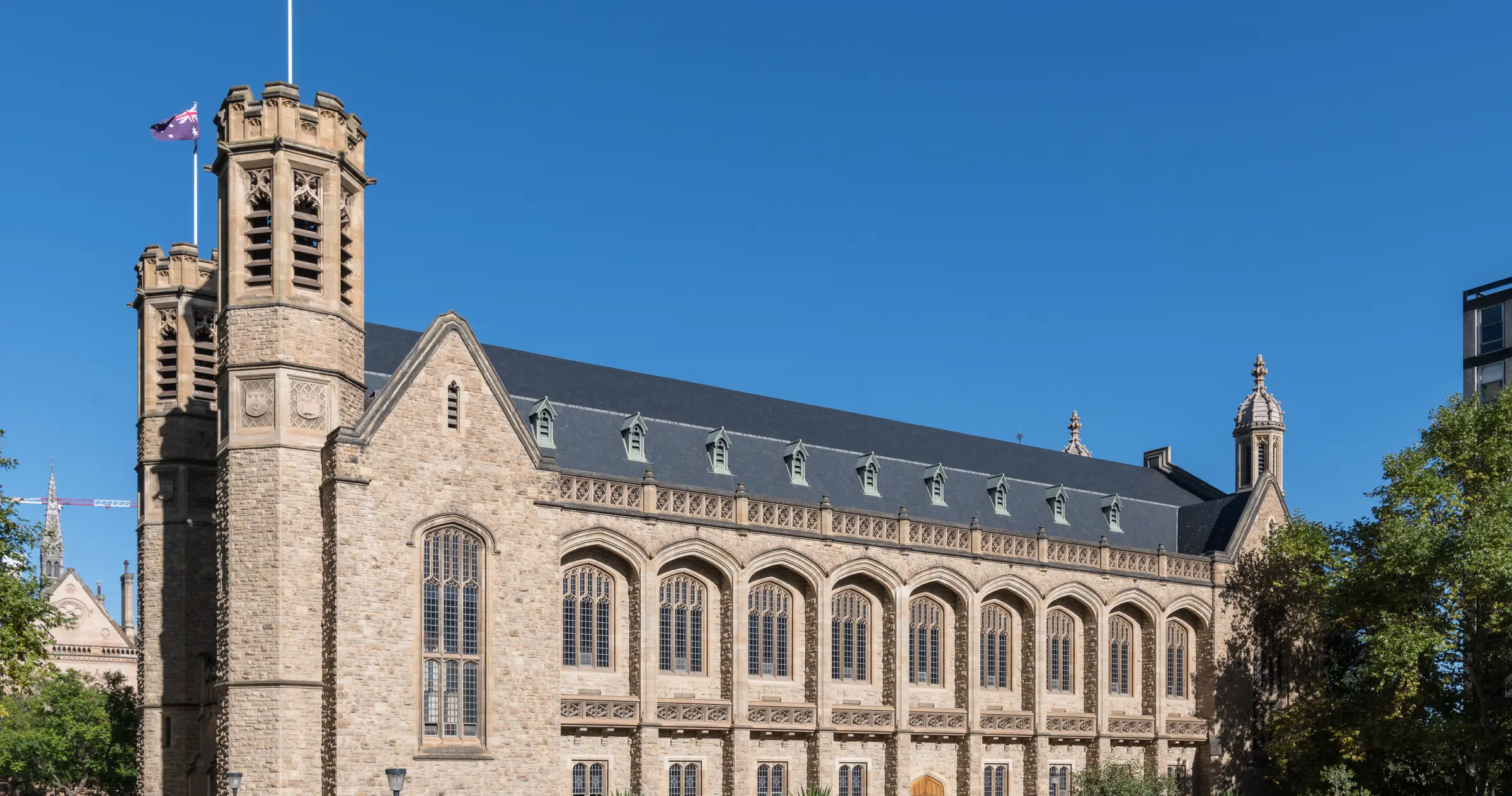 Bonython Hall on North Terrace, its sandstone bell tower, gable and tall arched windows under a slate roof and a clear blue sky